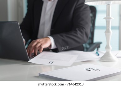 Scale And Justice Sign On Pile Of Paper. Lawyer Working In Office. Attorney Writing A Legal Document With Laptop Computer. Law Firm And Business Concept.