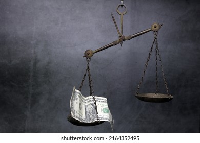A scale made of brass with an empty 1 dollar bill.  tilt the scale  black tone cement background  The concept is like an injustice in the use of legal regulations.  When money intervenes - Shutterstock ID 2164352495