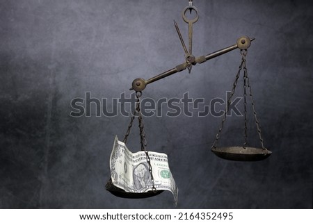 A scale made of brass with an empty 1 dollar bill.  tilt the scale  black tone cement background  The concept is like an injustice in the use of legal regulations.  When money intervenes