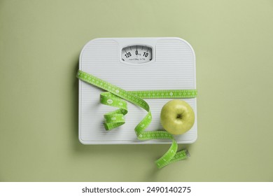 Scale tied with measuring tape and fresh apple on olive background, top view - Powered by Shutterstock