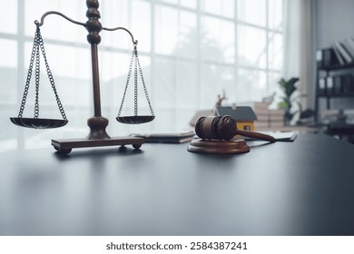 Escalas de justicia: Un mazo de madera descansa junto a una casa en miniatura y un conjunto de escalas de justicia en el escritorio de un abogado, simbolizando la imparcialidad y la equidad del sistema legal.  
