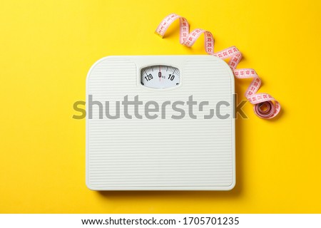 Scales and measuring tape on yellow background. Weight loss concept