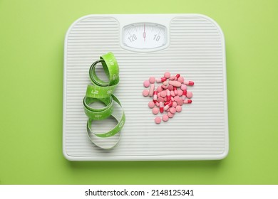 Scales With Weight Loss Pills And Measuring Tape On Green Background, Top View