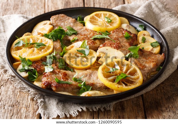 Scaloppini tender veal cooked with mushrooms and\
lemons in a spicy sauce close-up in a frying pan on the table.\
horizontal, rustic\
style\
