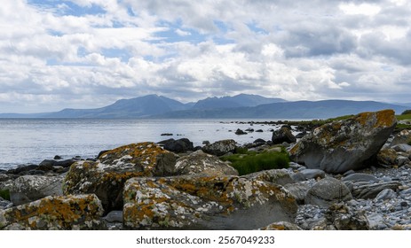 Scalpsie Bay, Isle of Bute, Scotland, June 8, 2024. Coastal view of rocky shores with distant mountains under a partly cloudy sky. A serene scene highlighting Scotland's natural beauty. - Powered by Shutterstock