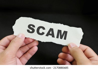 Scammed Victim Concept. Hand Holding A Piece Of Paper With Word Scam In Dark Black Background.