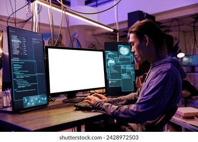 Scammer hacking using computer with empty white screen in abandoned warehouse. Asian criminal coding malicious software and doing illegal activities on monitor with blank display mockup