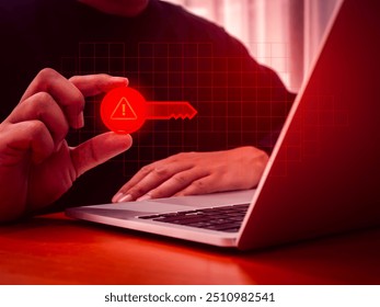 Scammer scam, digital identity theft, cybercrime online concept. Digital key with warning sign holding by hacker's hand on data network screen while using laptop computer in dark room, red tone.
