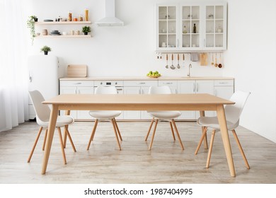 Scandinavian classic white kitchen with wooden details, minimalistic interior design. Modern furniture with accessories and various utensils, table and chairs in dinning room, copy space