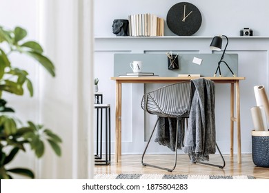 Scandinavian home office interior with wooden desk, design chair, wood panleing with shelf, plant, table lamp, carpet, office supplies and elegant accessories in modern home decor.