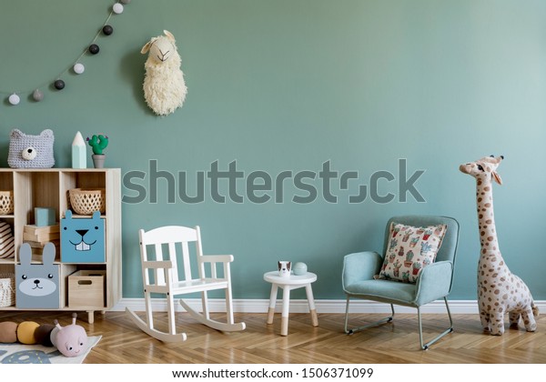 Scandinavian interior design of playroom with\
wooden cabinet, armchairs, a lot of plush and wooden toys. Stylish\
and cute childroom decor. Eucalyptus background walls. Copy space. \
Template.