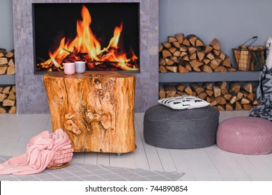 scandinavian interior with a fireplace, stump table, a pile of logs for fire and knitted padded stool