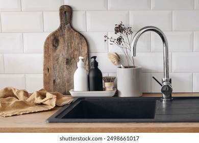 Scandinavian kitchen interior. Wooden countertop, chopping board. Soap, detergent dispenser glass bottles mockup. Dish brush, black sink. Eco dish washing concept, white wall, metro tiles background - Powered by Shutterstock