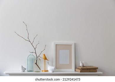 Scandinavian style. A bottle of water with a branch, two empty bottles of different shapes, figurines of birds are on a white fireplace. Copy space
