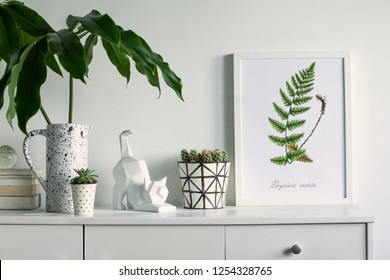 Scandinavian stylish cupboard with mock up poster frame, cat figure, tropical leaf, accessories, books, cacti. White background wall.