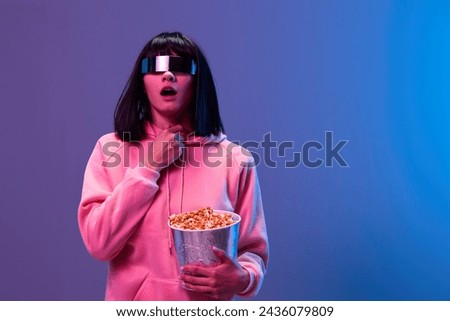 Scared awesome brunet woman in pink hoodie trendy specular sunglasses with popcorn hold hand on chest posing isolated in blue violet color light background. Neon party Cinema concept. Copy space