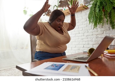 Scared Black Woman Looking On Spilled Coffee Or Tea From Cup On Laptop Computer During Working At Home Workspace. Concept Of Freelance And Remote Work. Young Millennial Girl Sitting At Wooden Table