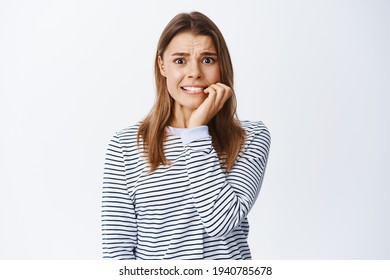 Scared blond girl biting nails on fingers and frowning, afraid of someone will know her little secret, standing anxious and panicking, white background - Shutterstock ID 1940785678