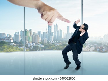 A Scared Businessman  In A Scare Pose And A Giant Hand Pointing At Him, On The Office Background. Business And Management, Employment Issues Or Getting Fired. 