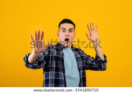 Scared Caucasian guy shouting in panic, making STOP gesture with both hands over orange studio background
