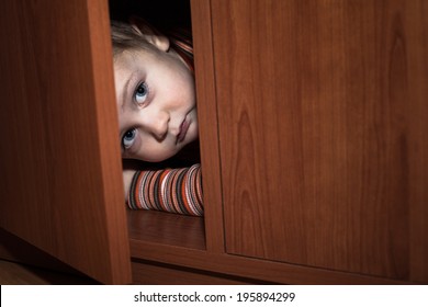 Scared child boy hiding in wardrobe