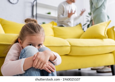 Scared child looking at camera while parents quarrelling on blurred background