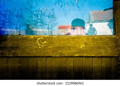 A Scared Child Looking Through A Hole In A Curtain