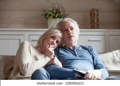 Scared Confused Attractive Blond Wife Sitting On Couch With Grey Haired Husband Watching Thriller Movie Cinema. Married Middle Age Couple Spending Free Time Looking Tv Show Or Program Feels Frightened