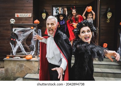 Scared Couple In Halloween Costumes Screaming While Running Out House From Creepy Kids