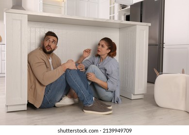 Scared Couple Hiding Under Table In Kitchen During Earthquake