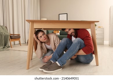 Scared Couple Hiding Under Table In Living Room During Earthquake