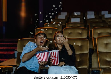 Scared Couple Jumping On Seats In Movie Theater. Handsome Man And His Girlfriend Spilling Popcorn From Box While Watching A Film In Cinema.  Surprised Thriller Film