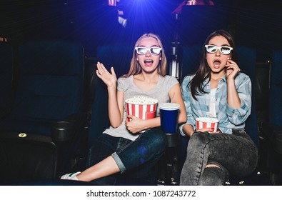 Scared and excited girls are sitting in a cinema hall and watching movie. They are amazed. Also girls have baskets of popcorn and a big cup of cola. - Powered by Shutterstock