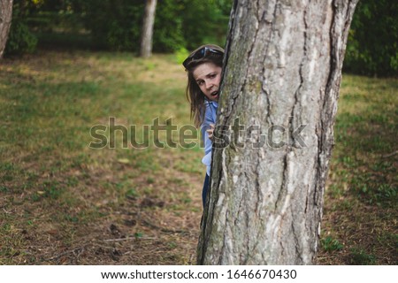 Scared girl hiding behind a tree trunk - Frightened caucasian woman peeking while being outside in a forest