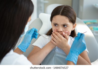 Scared Girl Sitting In Dental Chair Covering Mouth With Hands