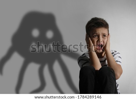 Scared little boy suffering from sciophobia and shadow behind him. Irrational fear of shadows