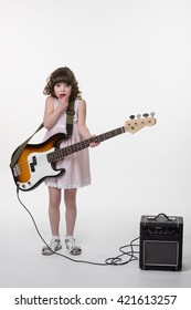 Scared Little Princess With Huge For Her Bass Guitar. Opened Mouth And Big Eyes. Small Special Amp In The Corner. Small Child Made A Mistake While Playing The Instrument. Isolated.