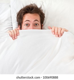 Scared Man Hiding In Bed Under The Sheets. Funny Concept Image With Young Caucasian Male Model Home In Bed.