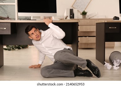 Scared Man Hiding Under Office Desk During Earthquake