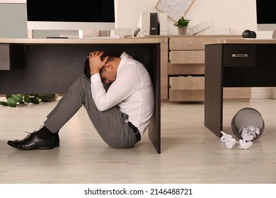 Scared Man Hiding Under Office Desk During Earthquake