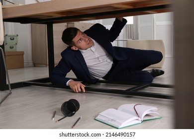 Scared Man Hiding Under Office Desk During Earthquake