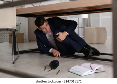 Scared Man Hiding Under Office Desk During Earthquake