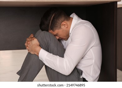 Scared Man Hiding Under Office Desk During Earthquake