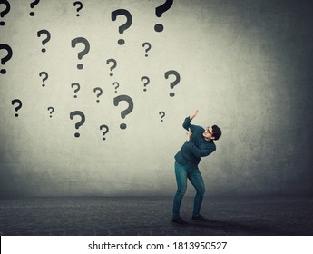 Scared man keeps hands raised up to protect him from multiple questions threat falling above him as numerous interrogation marks. Fear concept, person has no answers being under emotional pressure.