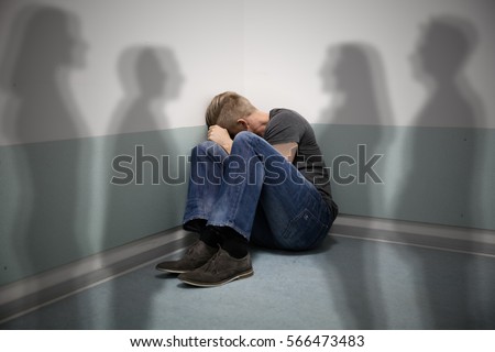Scared Man Sitting In The Corner Of A Room With People Shadows On Wall