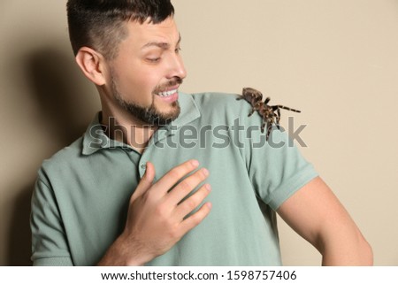 Scared man with tarantula on beige background. Arachnophobia (fear of spiders)
