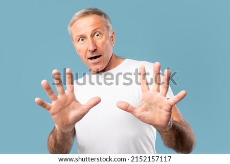 Scared mature guy showing stop gesture trying to defend himself, looking at camera and raising hands up, blue studio background, copy space. Human reactions and negative emotions concept