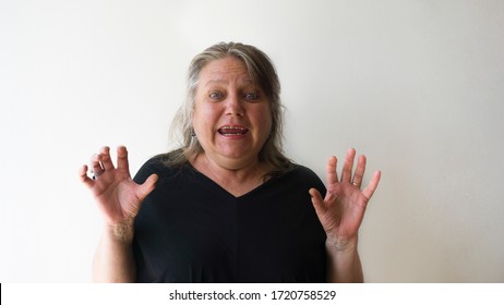 Scared Old Woman With Green Eyes Smiling At Camera. One Beautiful Green Eyed Elder Woman With Panic Attack Concept. Modern Blonde Lady With Casual Hair Isolated On White Wall Background.