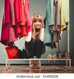 Scared Pretty Woman Hiding Among Clothes In Wardrobe. Attractive Young Girl Customer Shopping In Mall Shop. Fashion Clothing Sale Concept.