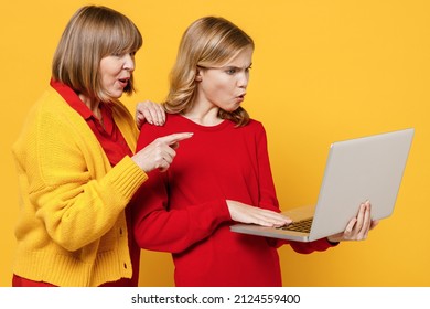 Scared Sad Woman 50s In Red Shirt With Teenager Girl 12-13 Years Old. Grandmother Granddaughter Hold Use Work Point On Laptop Pc Computer Isolated On Plain Yellow Background. Family Lifestyle Concept